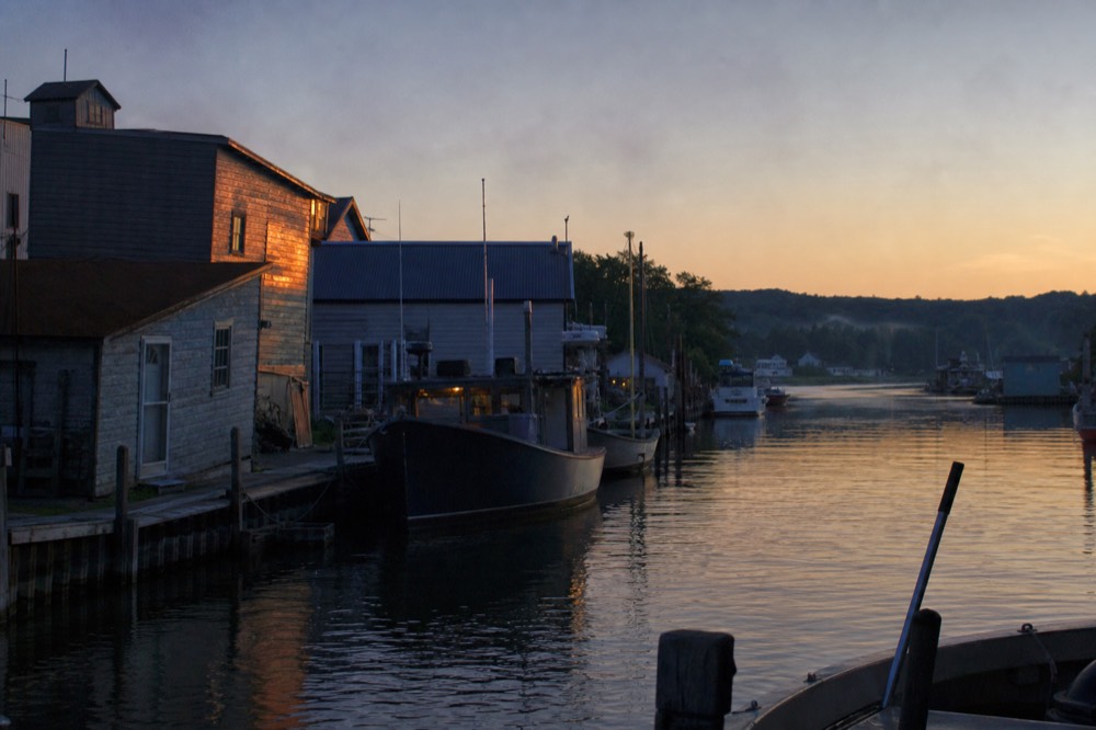 A quiet harbor channel at dusk with fishing boats and darkening water