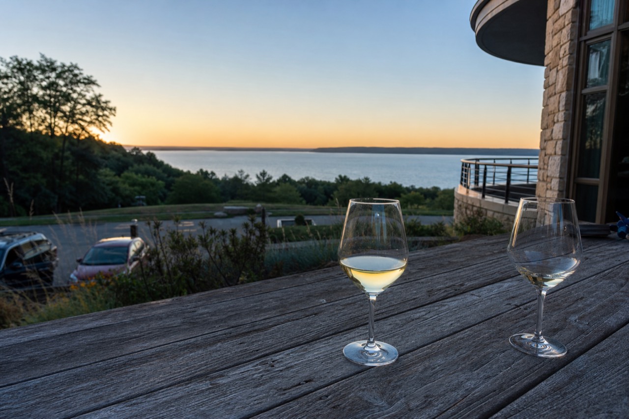Two wine glasses on a tasting room table overlooking a calm bay at dusk