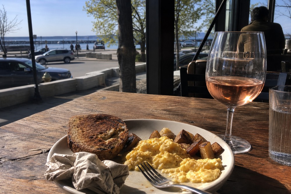 A plate of food set on a wooden restaurant table with a glass of wine beside it