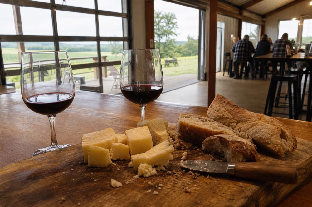 Wooden board with cheese, bread and two glasses of red wine on a tasting bar
