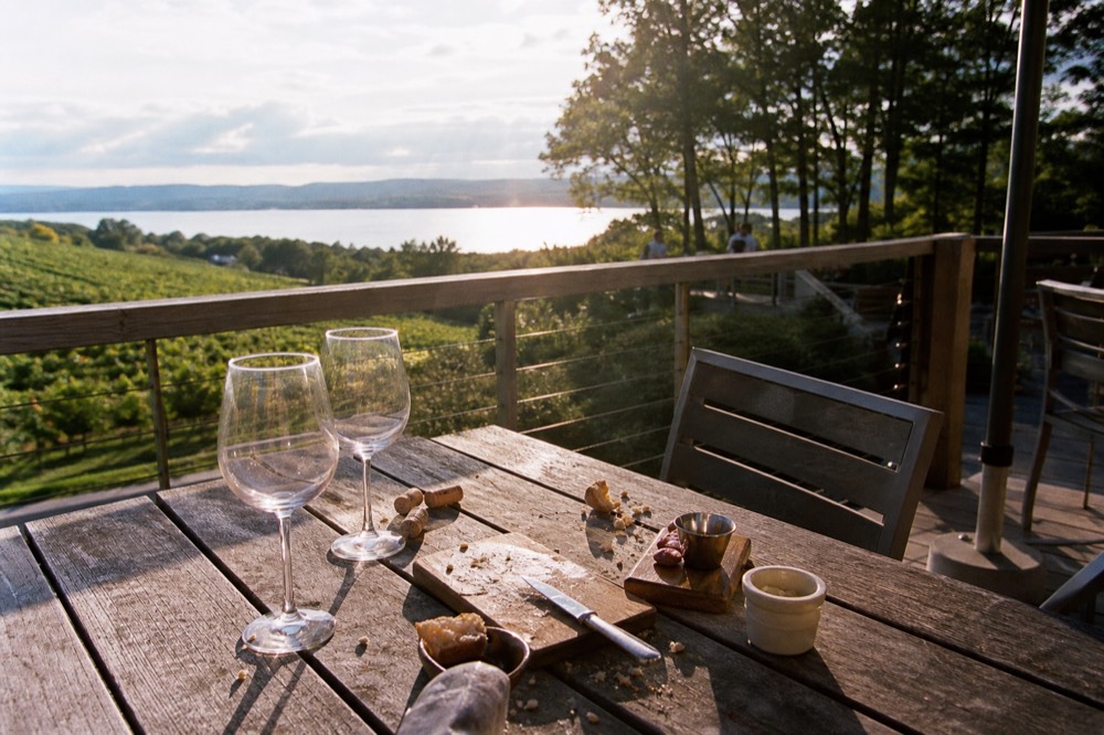 Two wine glasses on a patio table facing a wide blue bay