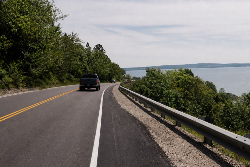 Coastline highway curving along a blue bay with wooded hills behind
