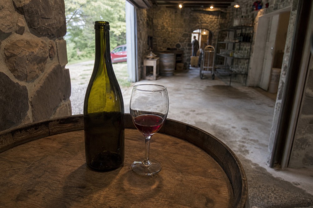 A bottle of wine and a tasting glass on a barrel top in a cellar