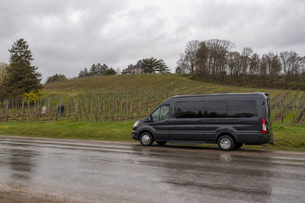 A shuttle van parked on a peninsula road with vineyards behind it