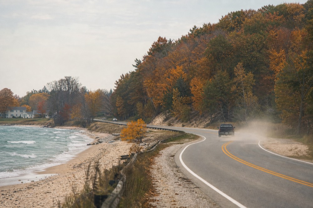 A winding lakeshore highway with water on one side and forested hills on the other