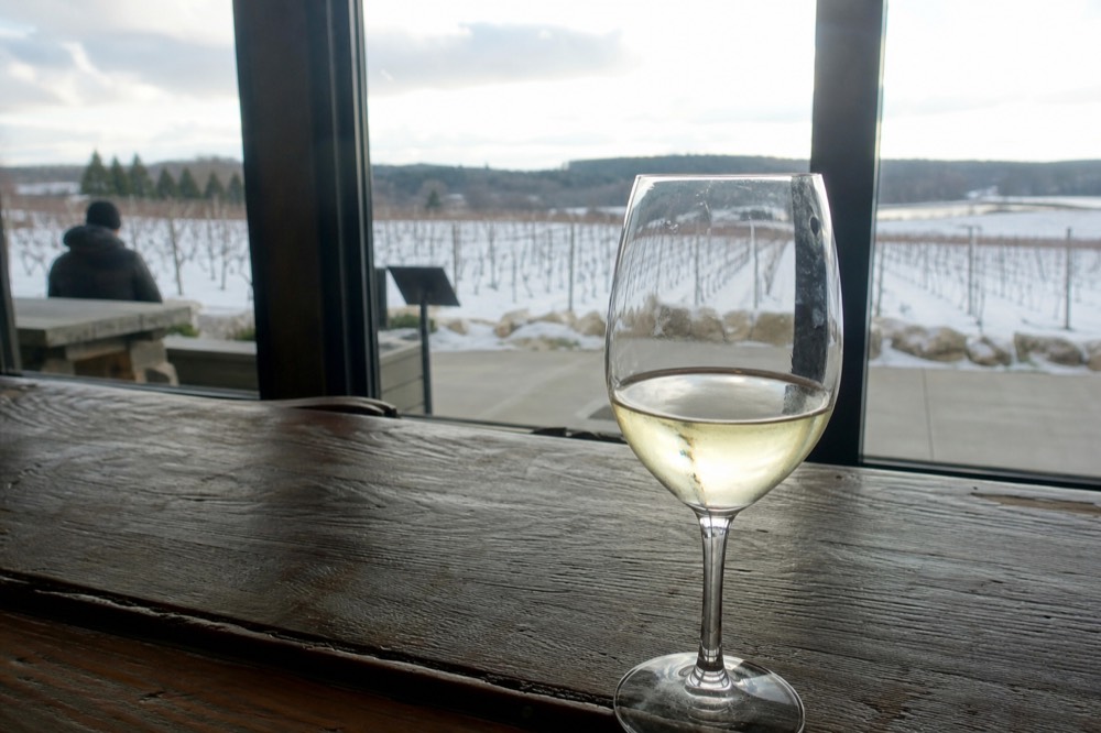 A single glass of white wine on a tasting room counter with vineyard light behind