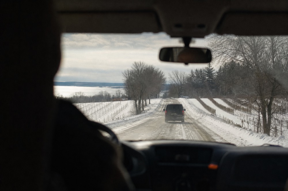 An enclosed tour vehicle on a snowy peninsula road between vineyards