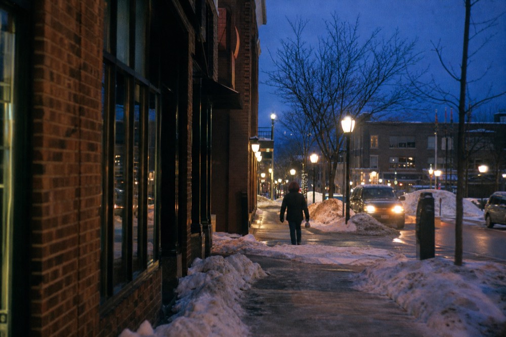 Downtown Traverse City storefronts glowing at dusk with snow on the sidewalks
